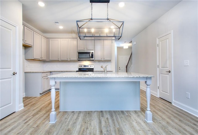 kitchen with stainless steel appliances, light stone counters, pendant lighting, a center island with sink, and light wood-type flooring