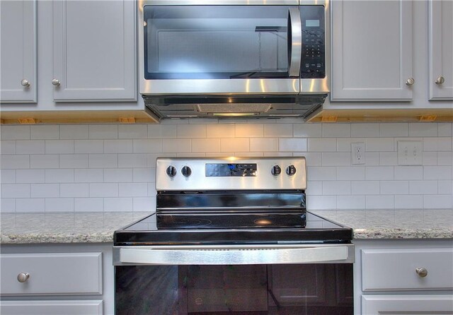 kitchen with light stone countertops, appliances with stainless steel finishes, backsplash, and white cabinetry