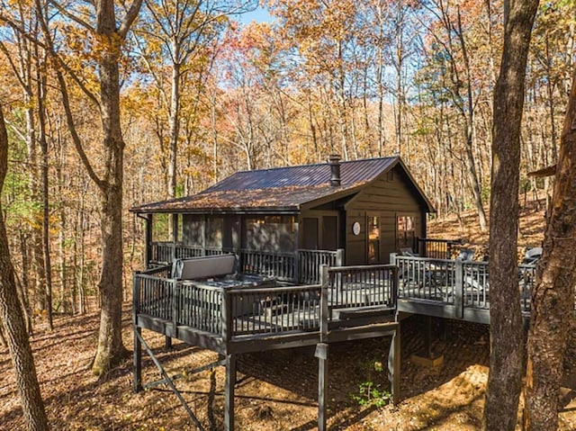 rear view of property featuring metal roof, a view of trees, and a wooden deck