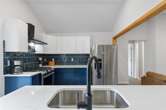 kitchen featuring lofted ceiling, wall chimney range hood, sink, blue cabinetry, and stainless steel appliances