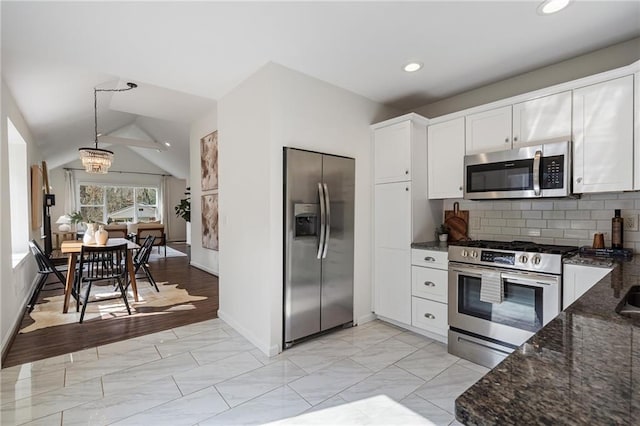 kitchen with white cabinetry, vaulted ceiling, dark stone countertops, appliances with stainless steel finishes, and decorative backsplash