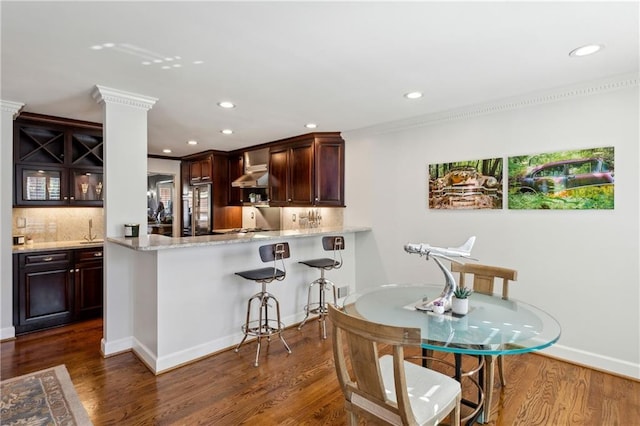 kitchen with high end fridge, backsplash, dark wood finished floors, a breakfast bar area, and wall chimney range hood