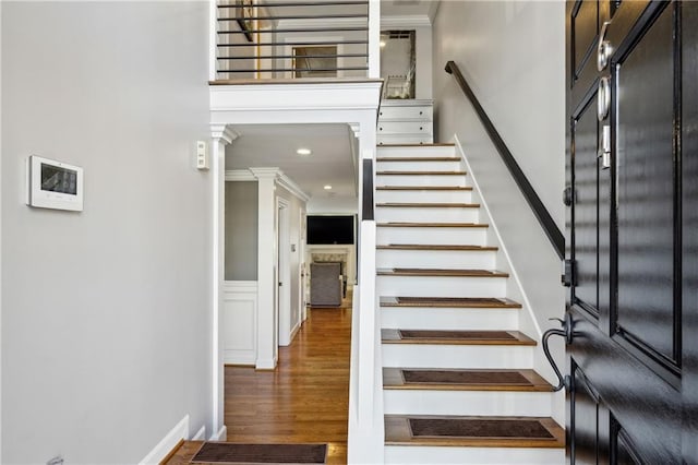 staircase featuring ornate columns, wood finished floors, a towering ceiling, and ornamental molding