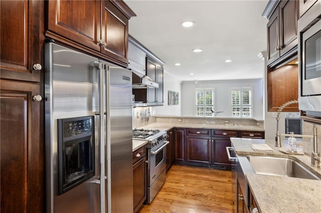 kitchen featuring light stone counters, wall chimney exhaust hood, crown molding, light wood finished floors, and high end appliances