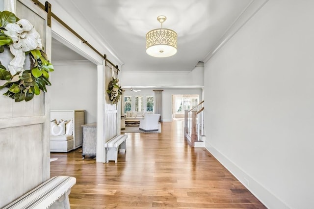 entryway with stairway, a barn door, ornamental molding, and wood finished floors