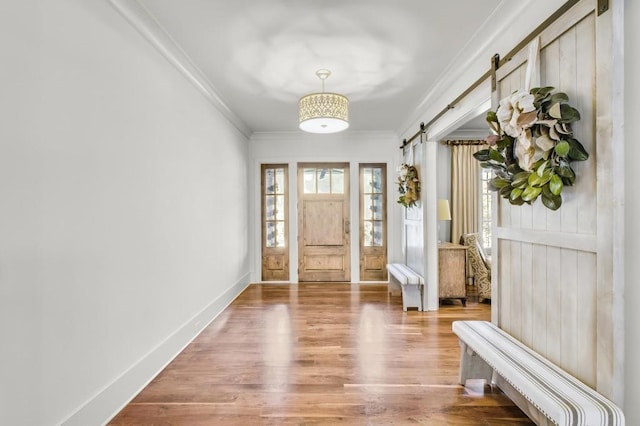 foyer entrance featuring plenty of natural light, a barn door, ornamental molding, and wood finished floors