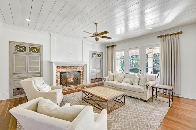 living room featuring baseboards, wooden ceiling, wood finished floors, crown molding, and a brick fireplace