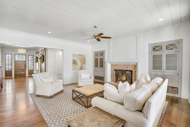 living room featuring recessed lighting, baseboards, light wood-style floors, ornamental molding, and a brick fireplace