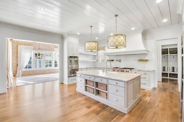 kitchen with pendant lighting, open shelves, appliances with stainless steel finishes, a kitchen island with sink, and white cabinetry