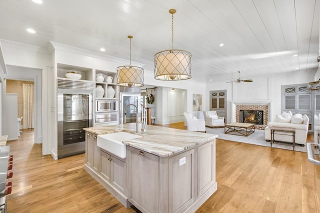 kitchen with a kitchen island with sink, stainless steel appliances, a sink, light stone countertops, and decorative light fixtures