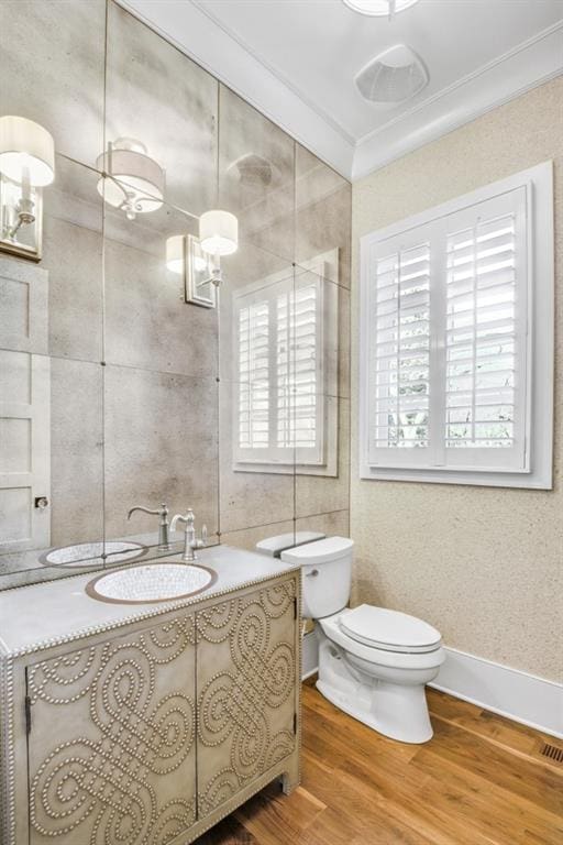 bathroom featuring toilet, wood finished floors, vanity, baseboards, and crown molding