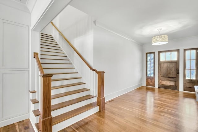 foyer with light wood finished floors, baseboards, stairs, and ornamental molding