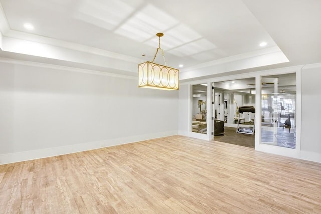 empty room featuring baseboards, crown molding, a tray ceiling, and wood finished floors