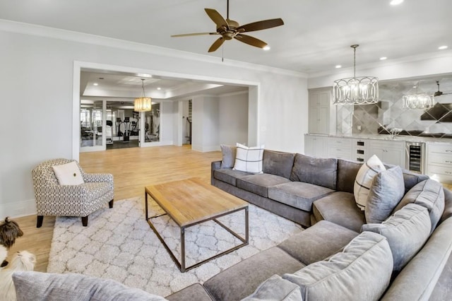 living area featuring light wood finished floors, beverage cooler, crown molding, a bar, and recessed lighting