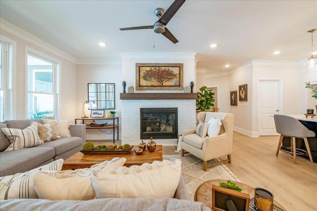 living room with light wood-type flooring, a brick fireplace, crown molding, and ceiling fan