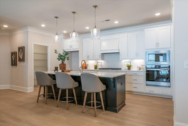 kitchen featuring stainless steel appliances, custom exhaust hood, white cabinets, and a kitchen island with sink