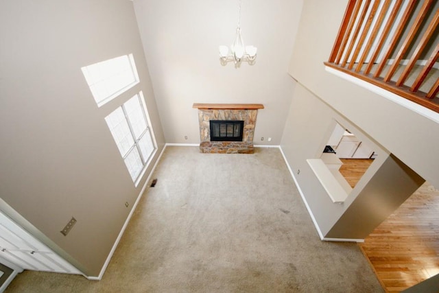 unfurnished living room featuring carpet floors, a towering ceiling, a stone fireplace, and a chandelier