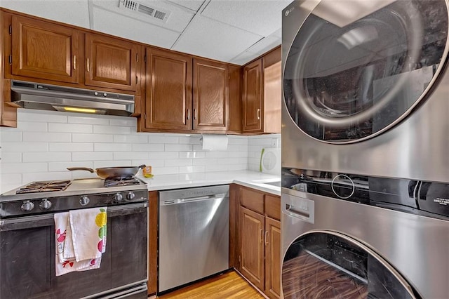 kitchen with backsplash, a drop ceiling, range with gas cooktop, stacked washer and clothes dryer, and dishwasher