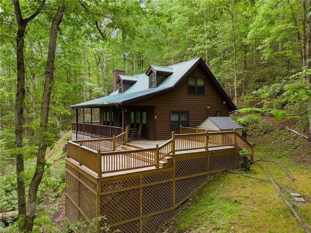 rear view of house featuring a deck, a chimney, metal roof, and a wooded view