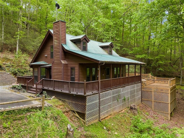 view of side of home featuring a deck, a chimney, metal roof, and a wooded view