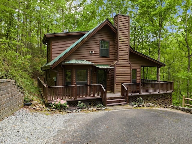 view of front facade with a forest view, a chimney, and a deck