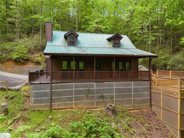 view of front of property featuring a porch, a view of trees, metal roof, and a chimney