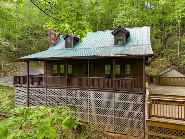 view of front of house with a chimney, covered porch, a wooded view, and metal roof
