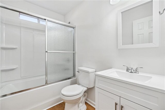 bathroom featuring toilet, bath / shower combo with glass door, wood finished floors, and vanity