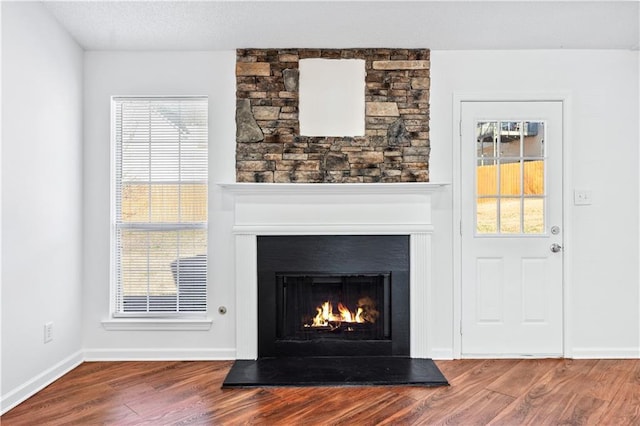 interior details featuring a warm lit fireplace, wood finished floors, and baseboards