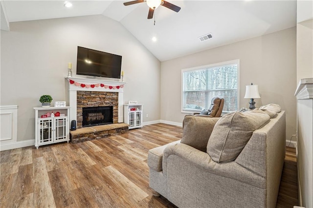 living room with lofted ceiling, hardwood / wood-style floors, a stone fireplace, and ceiling fan