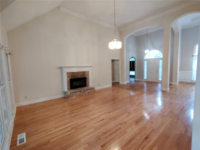 unfurnished living room with arched walkways, light wood-style flooring, a fireplace, and high vaulted ceiling