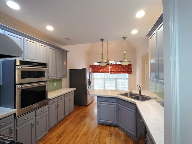 kitchen with light wood-type flooring, gray cabinets, a sink, stainless steel appliances, and light countertops