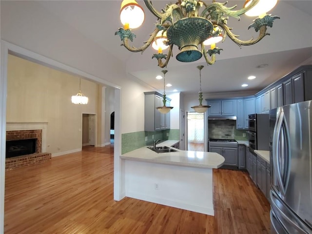 kitchen featuring gray cabinets, a sink, stainless steel appliances, a peninsula, and a fireplace