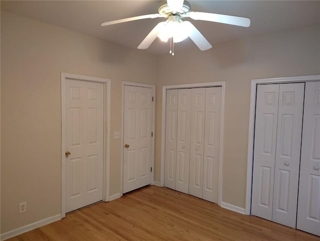 unfurnished bedroom featuring a ceiling fan, baseboards, light wood-type flooring, and two closets