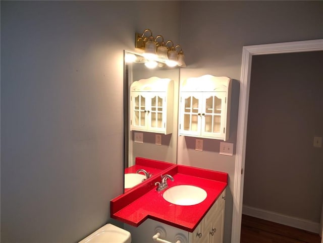 bathroom with toilet, vanity, baseboards, and wood finished floors