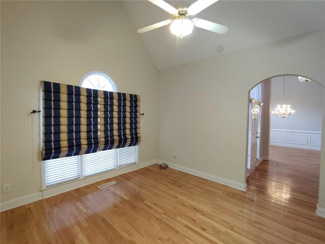 empty room featuring ceiling fan with notable chandelier, wood finished floors, visible vents, and arched walkways