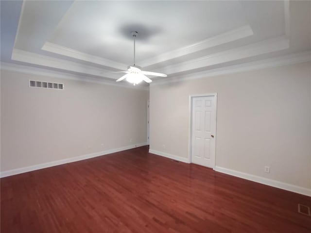 empty room featuring wood finished floors, visible vents, baseboards, crown molding, and a raised ceiling