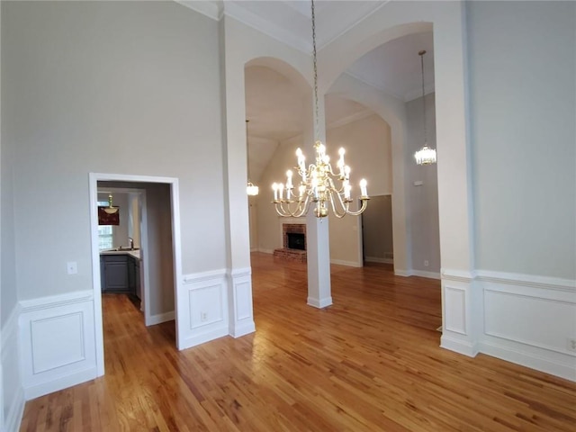 unfurnished dining area featuring a chandelier, light wood-style flooring, a fireplace, arched walkways, and a decorative wall