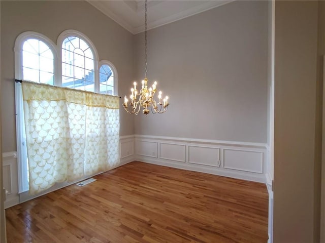 spare room featuring wood finished floors, visible vents, crown molding, a decorative wall, and a notable chandelier