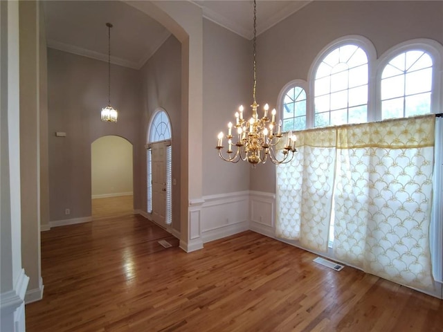 foyer entrance featuring wood finished floors, visible vents, arched walkways, and ornamental molding