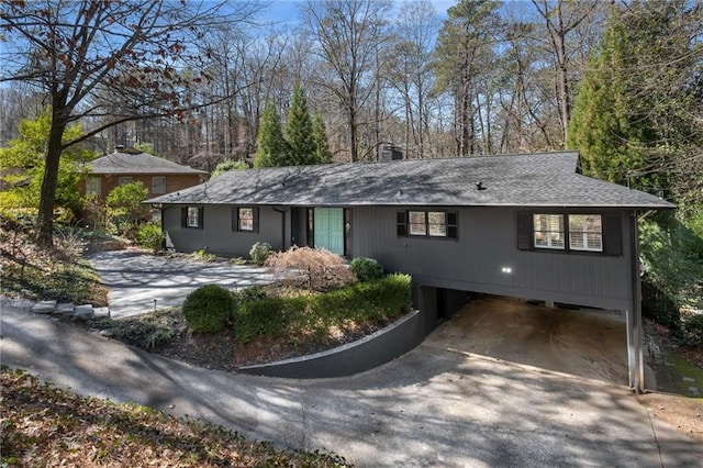 ranch-style house featuring concrete driveway, roof with shingles, and a chimney