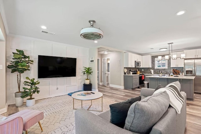 living area featuring light wood-type flooring, visible vents, crown molding, and baseboards