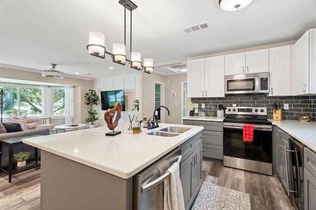 kitchen featuring a center island with sink, gray cabinets, light countertops, appliances with stainless steel finishes, and white cabinetry