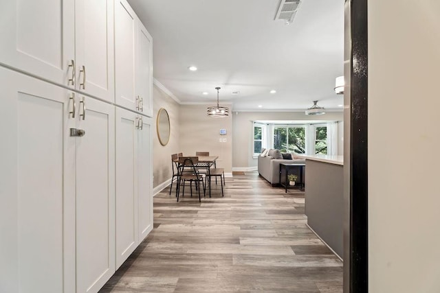 hall featuring light wood finished floors, baseboards, visible vents, ornamental molding, and recessed lighting