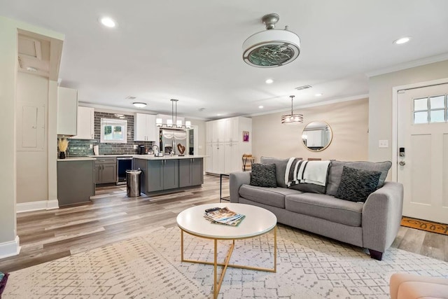 living room with light wood-type flooring, visible vents, crown molding, and recessed lighting