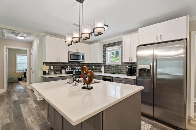 kitchen featuring appliances with stainless steel finishes, decorative light fixtures, a center island, light countertops, and white cabinetry