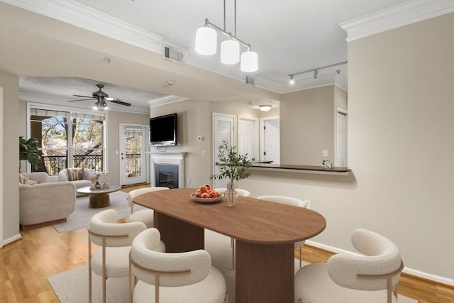 dining space featuring crown molding, light hardwood / wood-style flooring, rail lighting, and ceiling fan