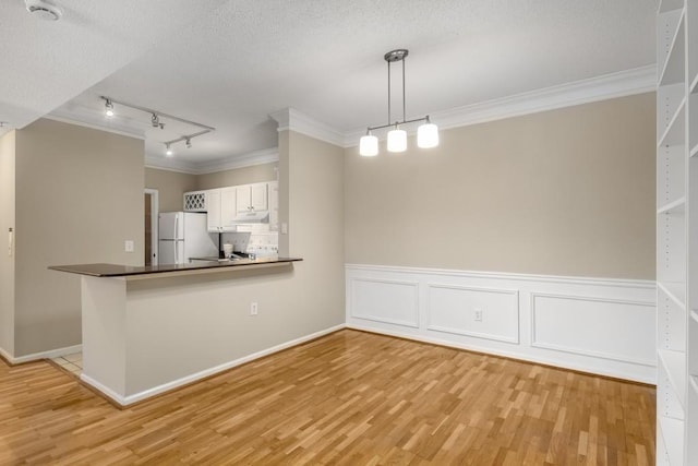 kitchen featuring track lighting, kitchen peninsula, white fridge, pendant lighting, and white cabinets