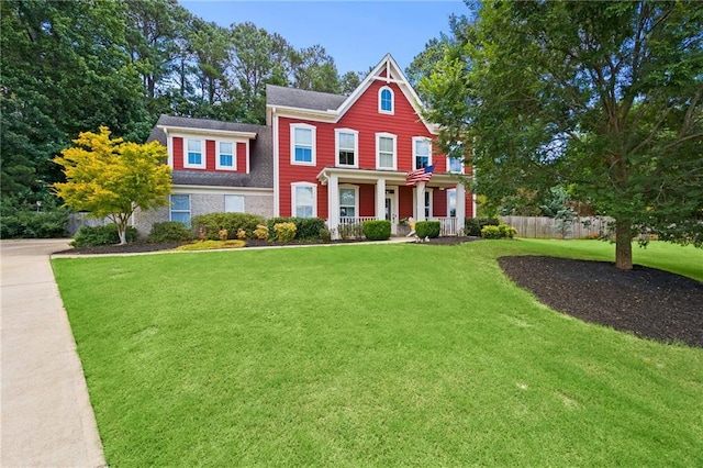 view of front facade featuring covered porch, a front lawn, and fence