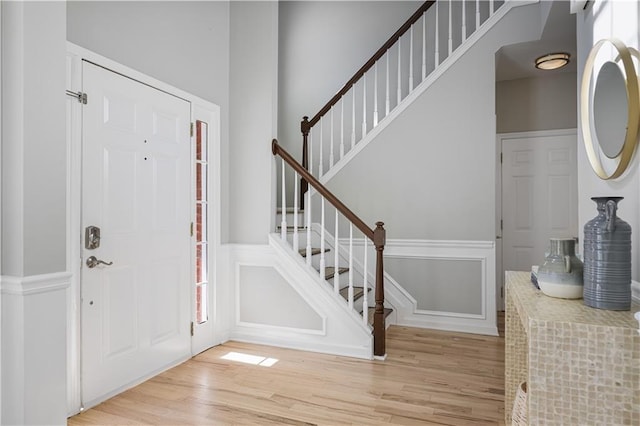 foyer with a wainscoted wall, stairs, light wood-style flooring, and a decorative wall